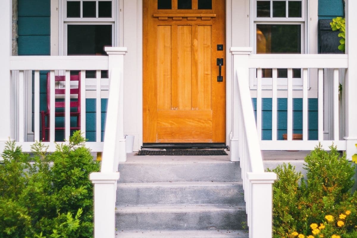 Covered front porch with a natural-finish craftsman wood door, white railing and teal lap siding
